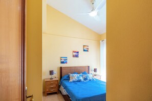 Ein Schlafzimmer mit Bett, Nachttischen, Deckenventilator und Wandbildern.