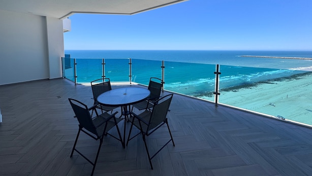 Un balcone con vista sull'oceano, un tavolo rotondo con sedie e un pavimento in legno.