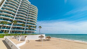 Un hotel sulla spiaggia con diversi balconi, una spiaggia sabbiosa e palme.