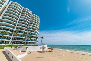 Ein Strandhotel mit mehreren Balkonen, einem Sandstrand und Palmen.