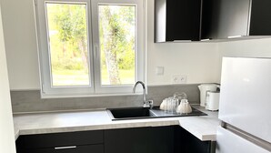 A modern kitchen with black cabinets, a white refrigerator, and a window with a view of greenery. - New house a stone's throw from the coastal path and harbours (Gujan-Mestras)