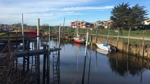 A calm water body with boats docked, a wooden pier, and houses in the background. - New house a stone's throw from the coastal path and harbours (Gujan-Mestras)