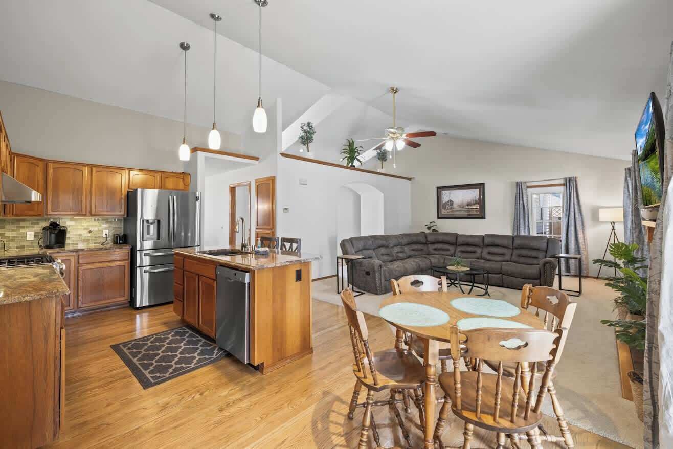 A modern kitchen with wooden cabinets, stainless steel appliances, and a dining area with a round table and chairs.