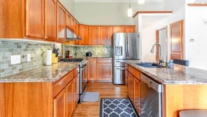 A modern kitchen with wooden cabinets, a stainless steel refrigerator, and a granite countertop.