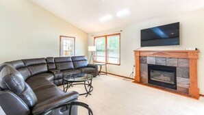 A living room with a sectional sofa, a fireplace, a flat-screen TV, and a ceiling fan.