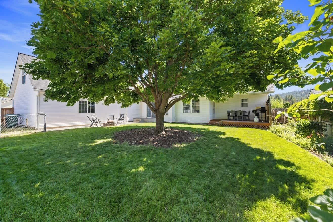 Una propiedad residencial con un césped cuidado, un árbol grande y una casa de techo inclinado.