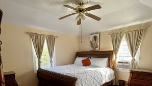 A bedroom with a wooden bed, a ceiling fan, and a window with curtains. - 3 bedroom home with pool (Sandys)