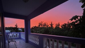 A balcony with a bench and railing, overlooking a sunset with trees in the background. - 3 bedroom home with pool (Sandys)