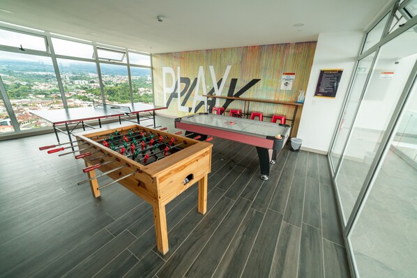 Een tafelvoetbal tafel en een pingpongtafel in een ruimte met grote ramen en uitzicht over de stad.