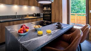 A modern kitchen with a marble countertop, a black pendant light, and a view of the outdoors through a large window. - Solly Nook - alpine holiday for 8, hot tub & close to action - OVO Network (Châtel)