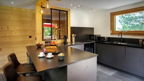 A modern kitchen with a central island, stainless steel appliances, and a large window. - Chalet Hychris - ski holiday between Annecy & the mountains - OVO Network (Alex)