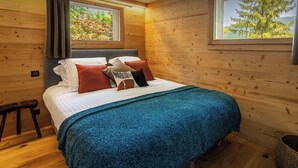 A wooden-paneled bedroom with a bed, pillows, and a view of trees through a window. - Chalet Hychris - ski holiday between Annecy & the mountains - OVO Network (Alex)