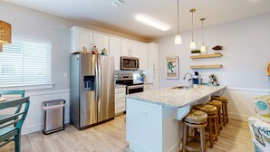 Una cocina moderna con un refrigerador de acero inoxidable, un microondas y un horno empotrado. Hay taburetes de bar y una pequeña isla con un lavamanos.