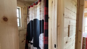 Un interior de madera con una cortina de ducha de estampado en blanco y negro, un tapete de cuadros y una ventana.