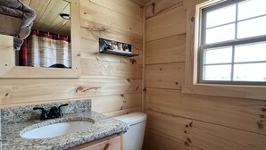 Un baño con paneles de madera, un lavabo de granito, un inodoro blanco, un espejo y una ventana.