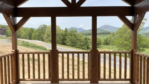 Una terraza de madera con ventilador de techo, barandillas de madera y vistas a un paisaje verde con montañas.