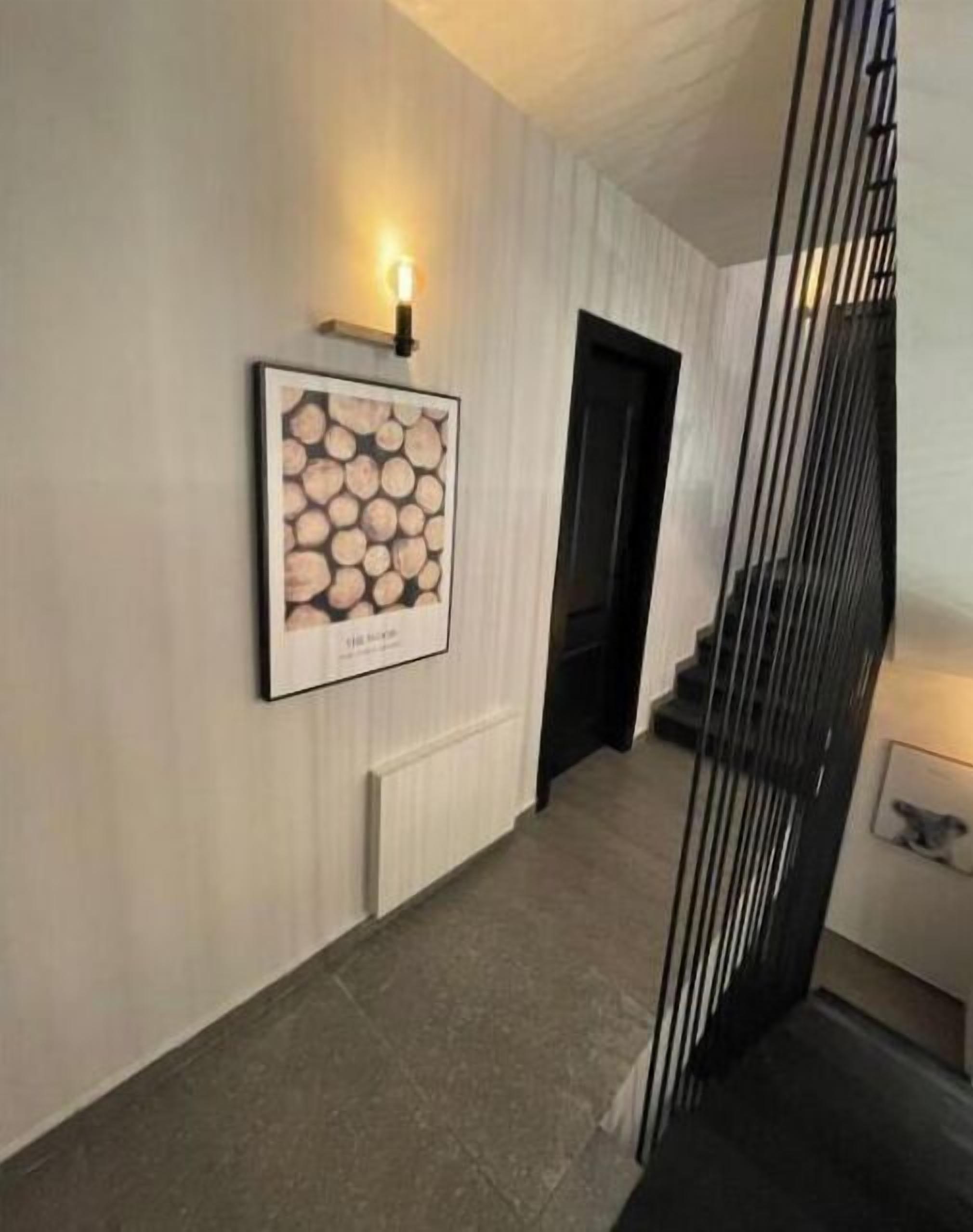 Un couloir orné d’un tableau encadré représentant des troncs d’arbres, d’un radiateur et d’un escalier avec une rampe noire.