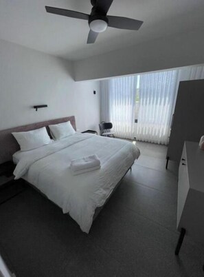 Quarto de hotel moderno com uma cama grande, um ventilador de teto, uma escrivaninha e uma cadeira.