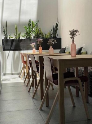 Uma sala de jantar com uma longa mesa de madeira, várias cadeiras e plantas em vasos.