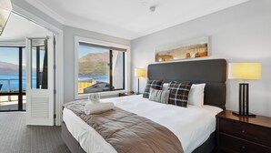 Une chambre d’hôtel avec un grand lit, une vue sur la mer, un tableau au mur et une table de chevet avec une lampe.