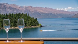 Une vue prise depuis un bateau, avec deux verres posés sur une table, un lac et des montagnes en arrière-plan.