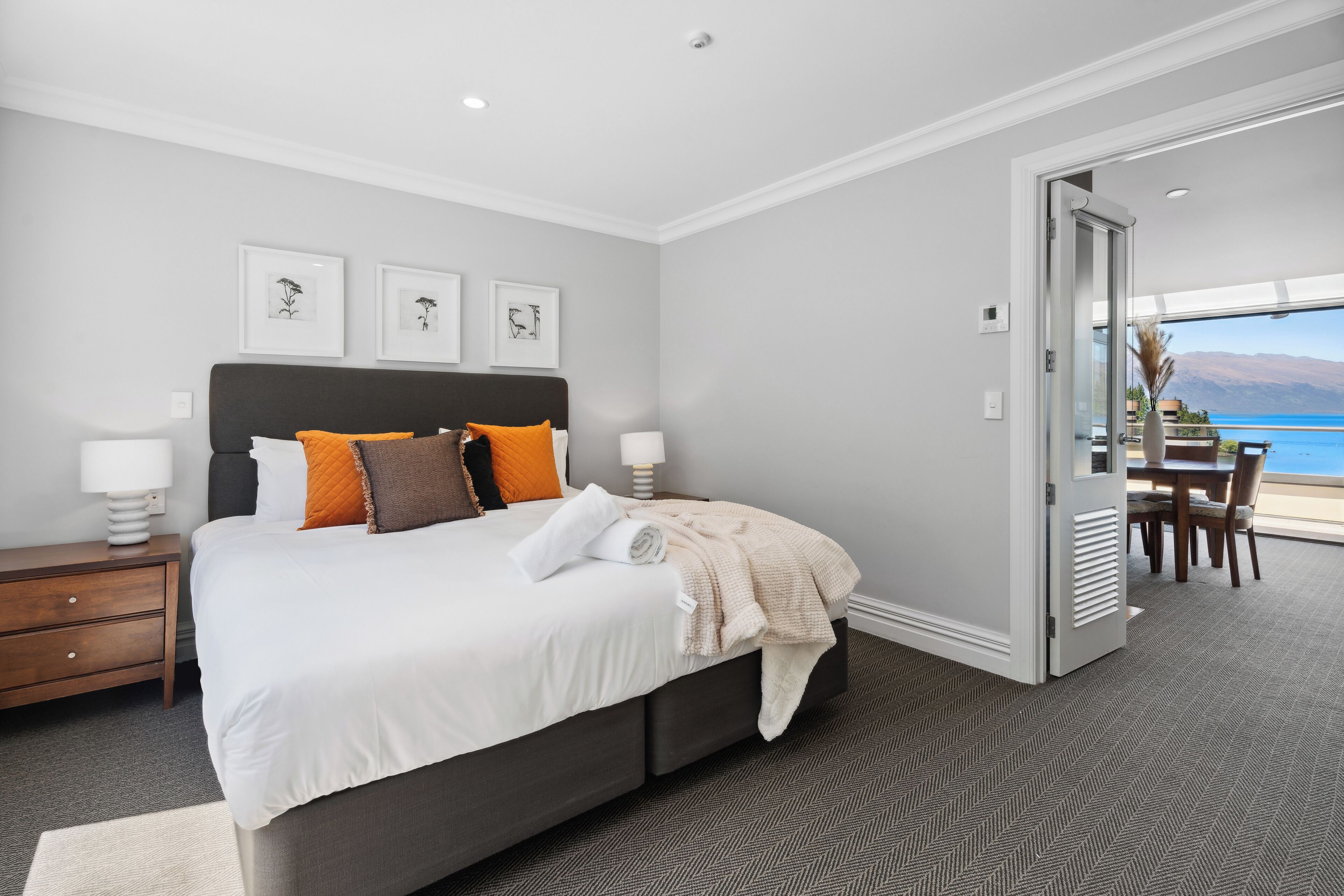 A modern bedroom with a large bed, a nightstand, and a view of the sea through an open door.