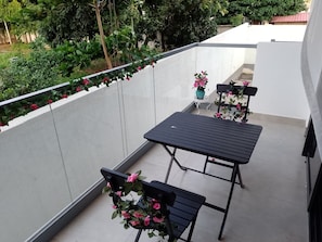 En balkon med et bord og stole, omgivet af en hvid mur og en have.