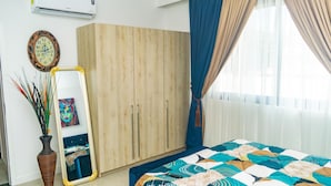 A bedroom with a large wardrobe, a mirror, a bed with a patterned bedspread, and a vase with plants.