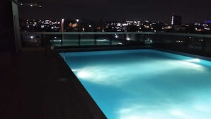 A rooftop pool with a cityscape view at night.