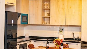 A modern kitchen with wooden cabinets, a black refrigerator, a microwave, and a dining area with a table set for two.