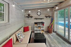 Una habitación acogedora con sofá, una mesita de centro, estanterías con adornos y vistas a una piscina.