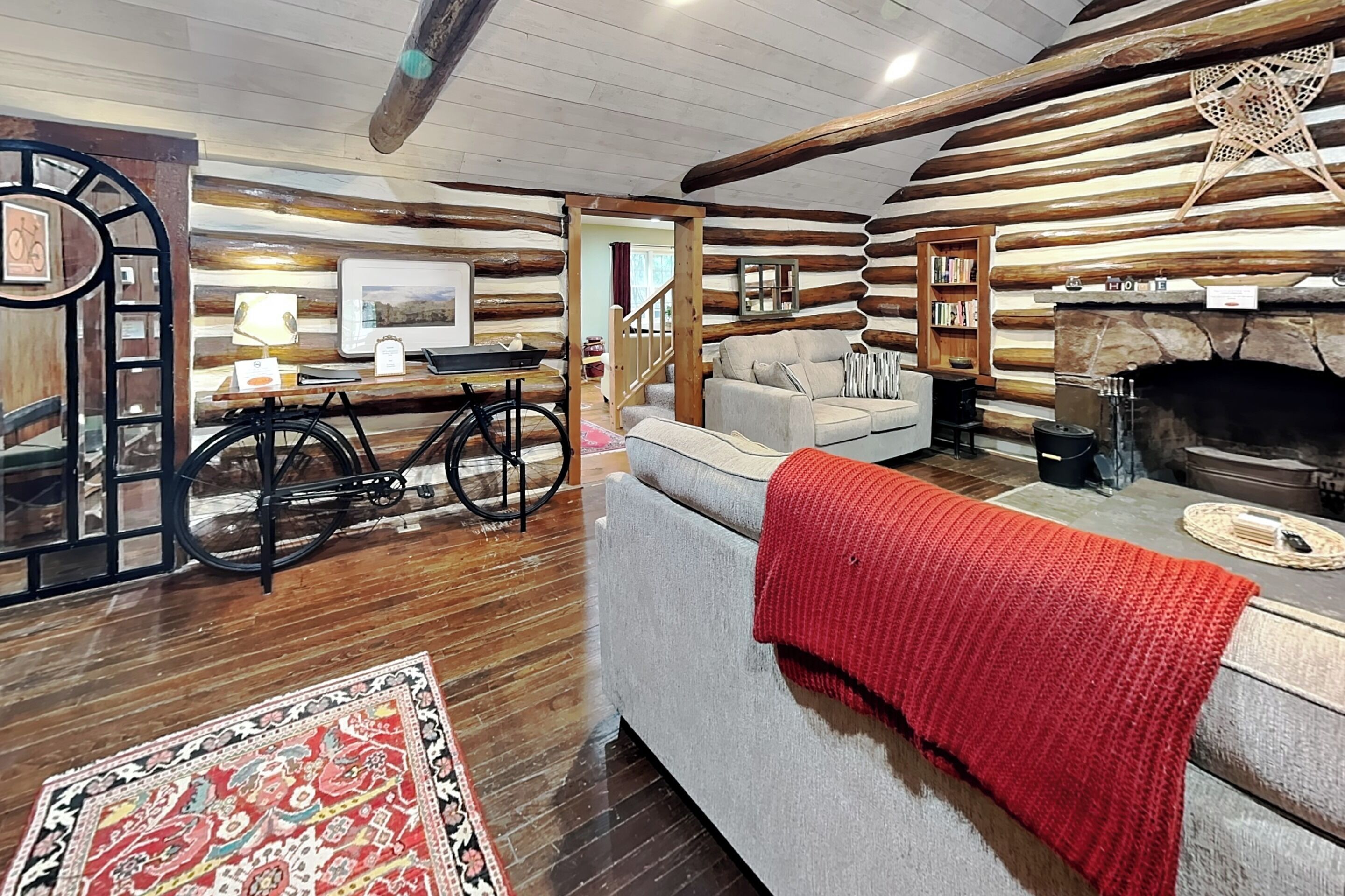 A log cabin interior with a sofa, a bicycle, a fireplace, and a bookshelf.