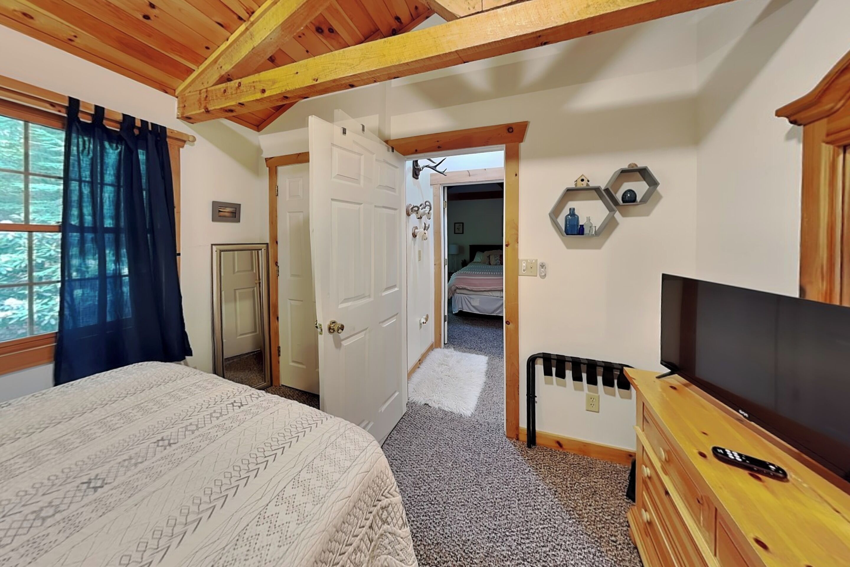 Un dormitorio con cama, televisor, cómoda y puerta que da a otra habitación.