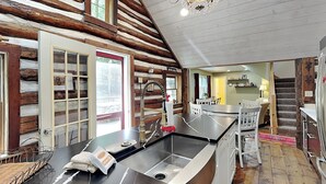 A log cabin interior with a kitchen area, wooden walls, a dining table, and a staircase. - Tucked Inn by Taylor Made Deep Creek (Swanton)