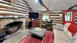 A log cabin interior with a stone fireplace, a television, a sofa, and a patterned rug. - Tucked Inn by Taylor Made Deep Creek (Swanton)