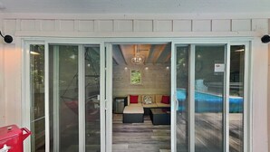 A sliding glass door entrance to a covered patio area with a wooden deck, a sofa set, and a hanging light fixture. - Tucked Inn by Taylor Made Deep Creek (Swanton)