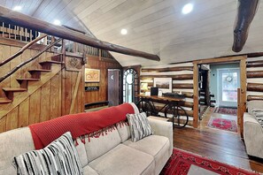 A cozy interior with a wooden staircase, a sofa with a red blanket, and a dining area with a bicycle.
