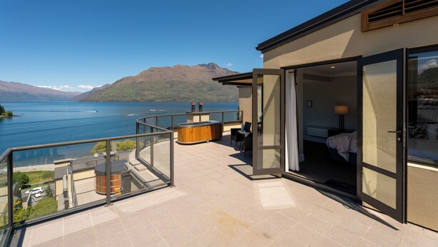 A balcony with a view of a lake and mountains, a wooden hot tub, and a glass door leading to a room. - SPACIOUS UNIT WITH VIEWS AND BALCONY (Queenstown)