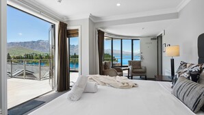 A hotel room with a large bed, a chair, a desk, and a view of a mountainous landscape and lake. - SPACIOUS UNIT WITH VIEWS AND BALCONY (Queenstown)