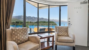 A room with a large window offering a view of mountains and a lake. There are two sofas and a small table with a remote control. - SPACIOUS UNIT WITH VIEWS AND BALCONY (Queenstown)