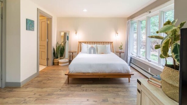 A bedroom with a wooden bed, large windows, and a view of greenery outside.