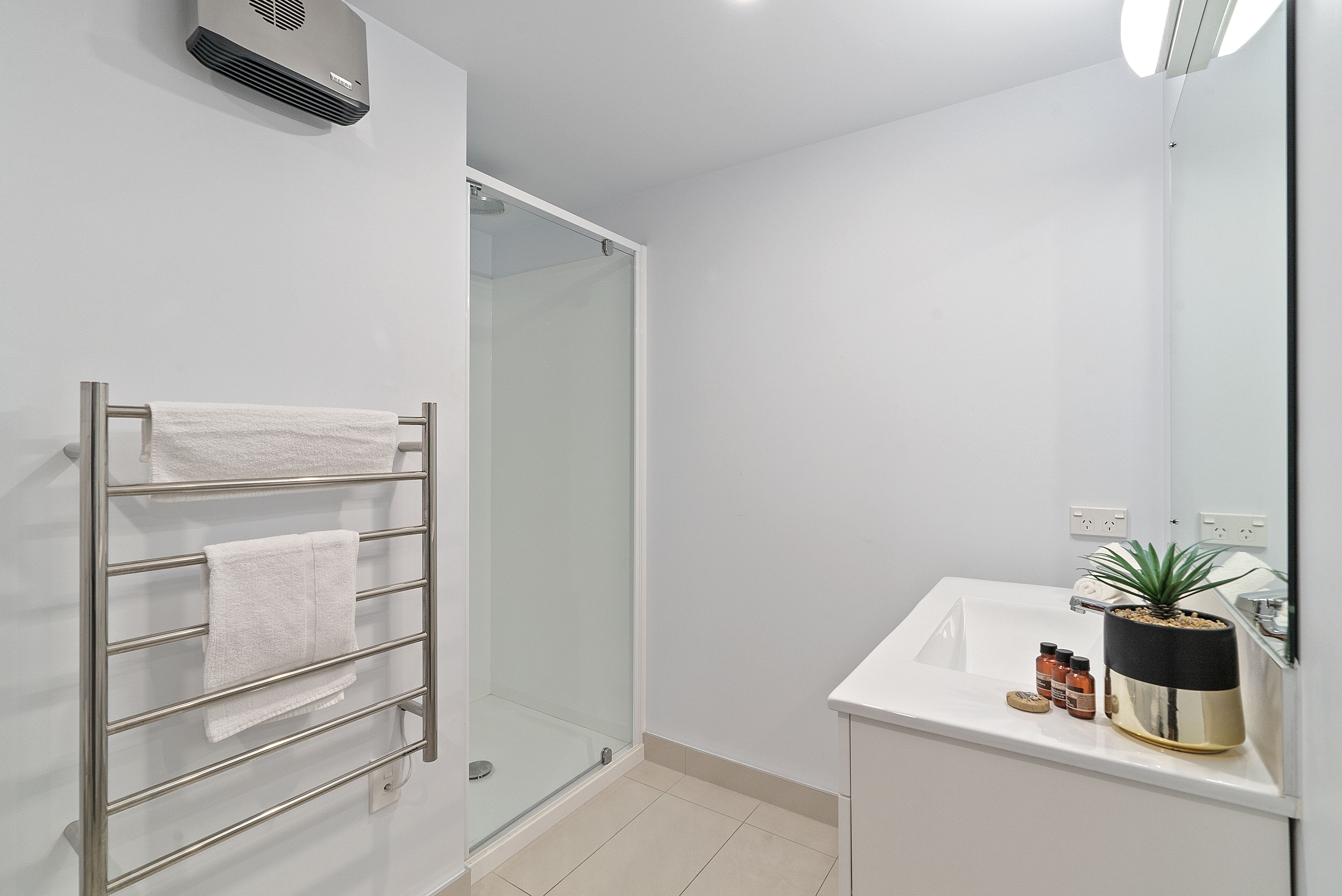 Een moderne badkamer met een douchecabine van glas, een wit wastafelmeubel met een potplant en een handdoekhouder met witte handdoeken.
