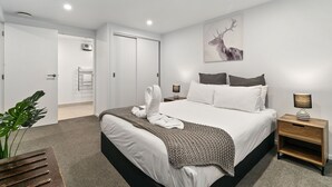Een moderne slaapkamer met een groot bed, nachtkastjes, een aan de muur bevestigd kunstwerk en een plant.