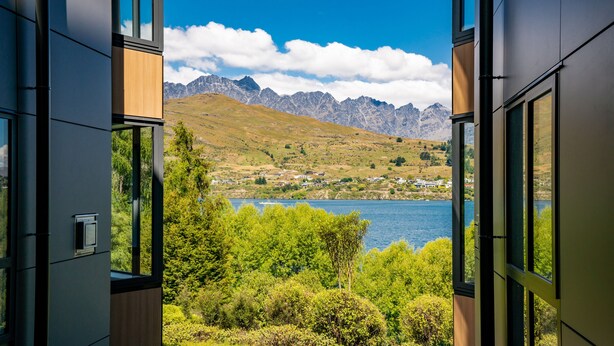 A modern building with large windows overlooking a lake and mountains. - LOVELY 2 BEDROOM APARTMENT WITH INDOOR FIREPLACE (Queenstown)