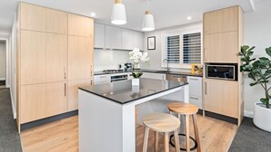 A modern kitchen with wooden cabinets, a central island with stools, pendant lighting, and a microwave. - LOVELY 2 BEDROOM APARTMENT WITH INDOOR FIREPLACE (Queenstown)