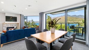 A modern living room with a stone fireplace, blue sofa, and a dining area with a wooden table and chairs. - LOVELY 2 BEDROOM APARTMENT WITH INDOOR FIREPLACE (Queenstown)