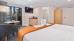 A hotel room with a bed, a desk with a chair, a TV, a shower, and a wardrobe. - LOVELY 2 BEDROOM APARTMENT WITH INDOOR FIREPLACE (Queenstown)