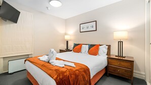 Une chambre d’hôtel avec un lit, deux tables de chevet, un téléviseur fixé au mur et une fenêtre avec des stores.