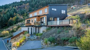 A modern two-story house with a balcony, situated on a hillside with a forested background. - A LUCKIE CHARM - 3-BEDROOM TOWNHOUSE WITH SPECTACULAR VIEW (Queenstown Hill)