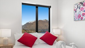 A hotel room with a bed, two red pillows, a white towel, and a painting on the wall. - A LUCKIE CHARM - 3-BEDROOM TOWNHOUSE WITH SPECTACULAR VIEW (Queenstown Hill)